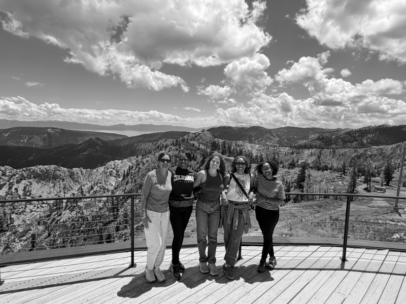 A photo of writers at the 2026 Community of Writers Summer Workshops in Olympic Valley. They are standing on a deck at High Camp with Lake Tahoe and the Sierras in the background. Photo by Sandra Rouse